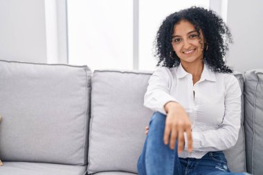 Evdeki kanepede kendinden emin gülümseyen genç İspanyol kadın.