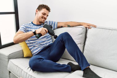 Evde perküsyon tabancası kullandığından emin bir şekilde gülümseyen İspanyol genç adam.