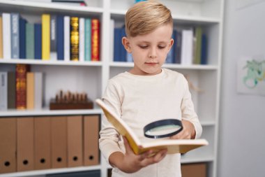 Sevimli çocuk sınıfta büyüteçle kitap okuyor.