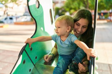 Anne ve oğlu parkta kayak yaparken kendinden emin bir şekilde gülümsüyor.