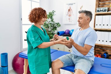 Orta yaşlı erkek ve kadın fizyoterapi üniforması giyip fizik tedavi kliniğindeki topları kullanarak rehabilitasyon seansı yapıyorlar.