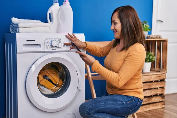 Middle Age Woman Turning Washing Machine Using Smartphone Laundry Room — Zdjęcie stockowe