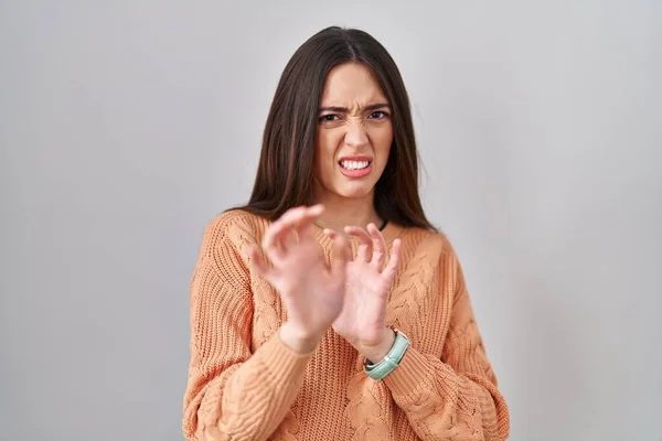 Young brunette woman standing over white background disgusted expression, displeased and fearful doing disgust face because aversion reaction.