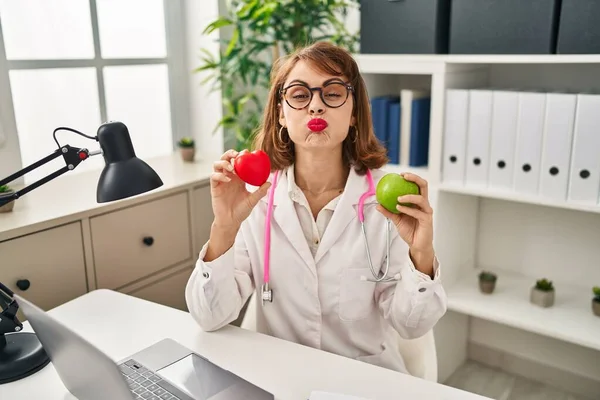 Young Doctor Woman Holding Heart Green Apple Puffing Cheeks Funny — Stock Photo, Image