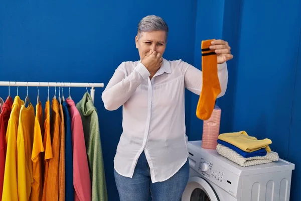 Middle Age Woman Smiling Confident Smelling Dirty Sock Laundry Room — ストック写真