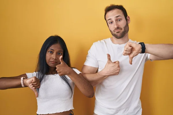 Interracial Couple Standing Yellow Background Doing Thumbs Disagreement Agreement Expression — 图库照片