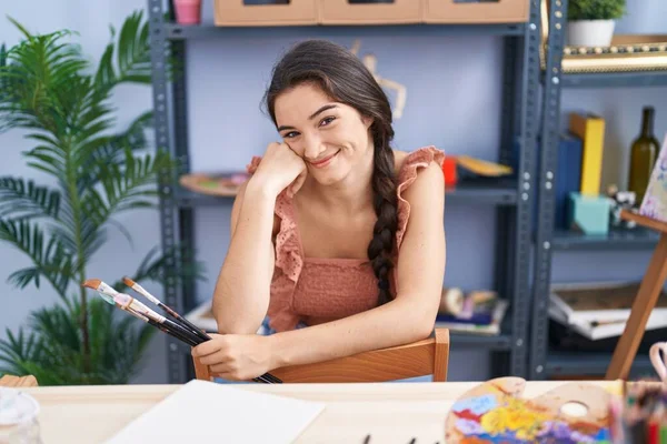 年轻的惊慌失措的女画家带着自信的笑容在艺术工作室里手握画笔 — 图库照片