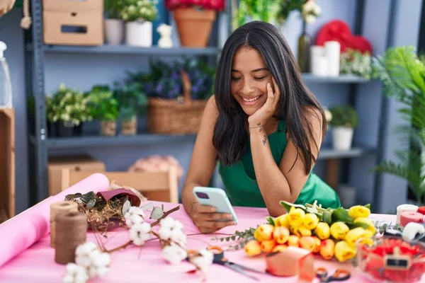 Young hispanic woman florist smiling confident using smartphone at florist shop