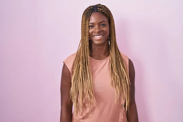 拥有辫子的非裔美国女人站在粉色的背景上 脸上挂着快乐而凉爽的笑容 幸运的人 — 图库照片