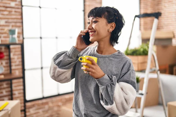 Young woman drinking coffee talking on the smartphone at new home
