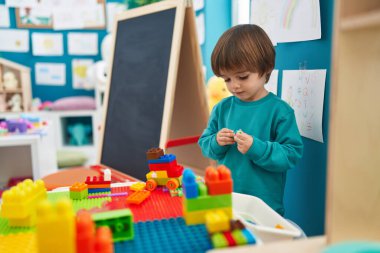 Adorable toddler playing with construction blocks standing at kindergarten