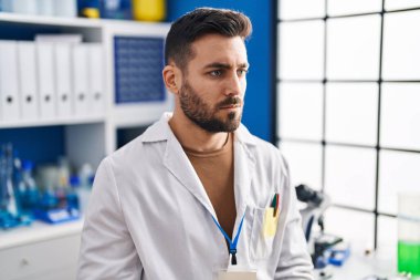 Laboratuvarda ciddi bir ifadeyle bilim adamı üniforması giyen İspanyol genç bir adam.