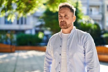 Genç beyaz adam parkta ciddi bir ifadeyle yan tarafa bakıyor.