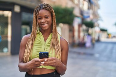 Afro-Amerikalı kadın sokakta akıllı telefon kullanarak kendine güveniyor.
