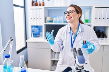 Young beautiful hispanic woman scientist using microscope speaking at laboratory