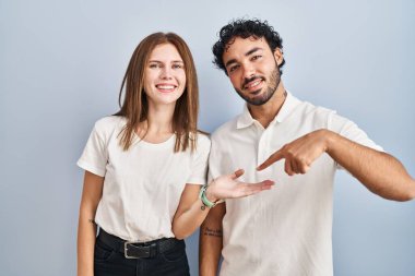 Gündelik giysiler giyen genç çift kameraya hayret içinde bakıp gülümserken elleri ve parmaklarıyla işaret ediyorlar.. 