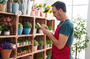 Çiçekçide akıllı telefon kullanan orta yaşlı bir çiçekçi.