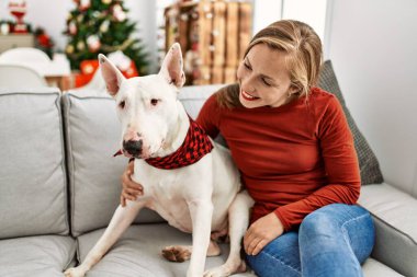 Beyaz bir kadın gülümsüyor kendine güvenen bir köpek evde Noel ağacının yanında oturuyor.