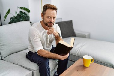 Orta yaşlı İspanyol adam evde kitap okuyor.