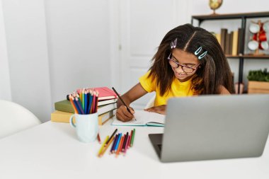 Afro-Amerikalı kız gülümseyerek evde ödevini yapıyor.