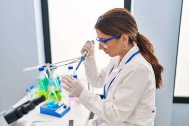 Laboratuvarda pipet kullanan, bilim adamı üniforması giyen İspanyol genç bir kadın.