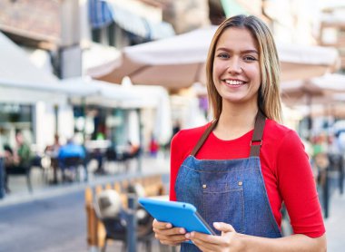 Kahve dükkanının terasında dokunmatik ped kullanarak gülümseyen genç İspanyol bayan garson.