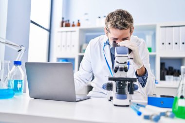 Young man scientist using laptop and microscope at laboratory