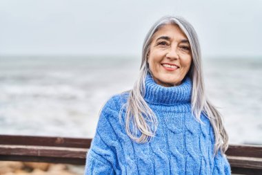 Orta yaşlı, kır saçlı, gülümseyen, kendine güvenen bir kadın.