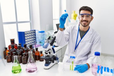 Laboratuvarda deney tüpü tutan bilim adamı üniforması giyen İspanyol genç adam.