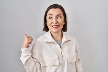 Orta yaşlı, ispanyol bir kadın, izole edilmiş arka planda gülümsüyor, gülümsüyor ve başparmağıyla yan tarafa bakıyor.. 