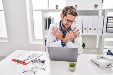 Hispanic man with beard wearing doctor uniform and stethoscope hugging oneself happy and positive, smiling confident. self love and self care 