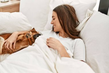 Genç İspanyol kadın yatak odasında köpeğe sarılıyor.