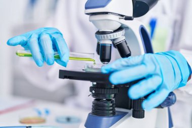 Laboratuvarda mikroskop kullanarak numuneye sıvı döken genç bir bilim kadını.