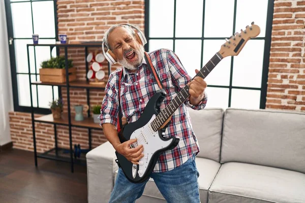 Senior grey-haired man singing song playing electrical guitar at home