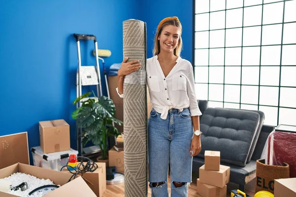 Young Blonde Woman Moving New Home Holding Rug Looking Positive — Stock Photo, Image