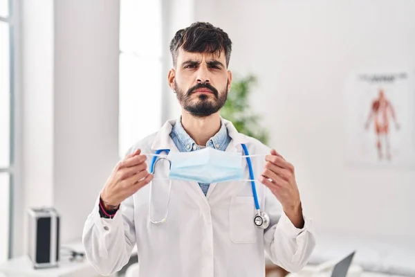 Young Hispanic Doctor Man Beard Holding Safety Mask Skeptic Nervous — Stockfoto