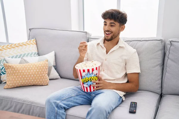 Young arab man eating popcorn watching movie at home