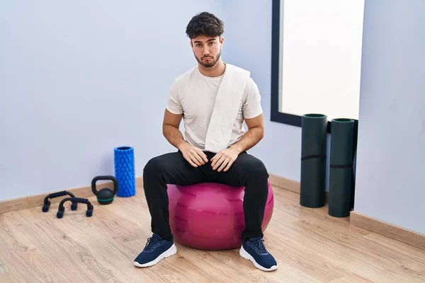 Hispanic man with beard sitting on pilate balls at yoga room depressed and worry for distress, crying angry and afraid. sad expression.