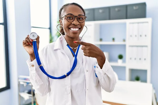 Black doctor woman holding stethoscope smiling happy pointing with hand and finger
