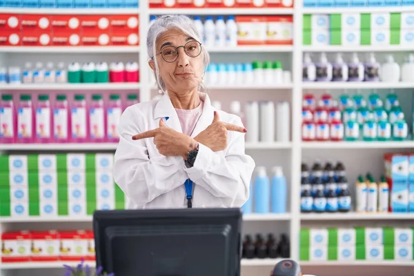 Middle age woman with tattoos working at pharmacy drugstore pointing to both sides with fingers, different direction disagree