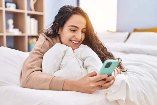 Young Hispanic Woman Using Smartphone Lying Bed Bedroom —  Fotos de Stock