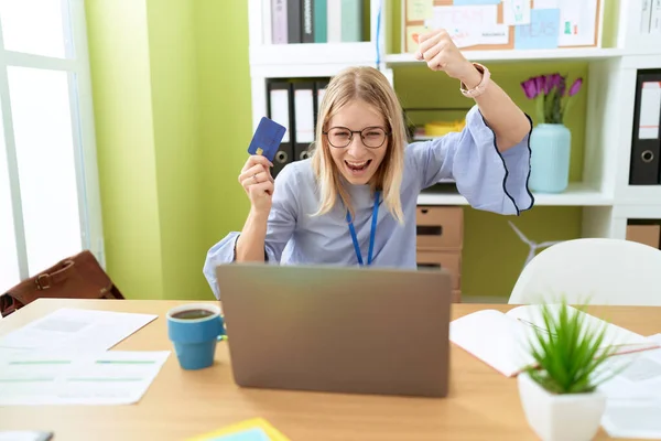 若いブロンド女性ビジネス労働者使用ラップトップとクレジットカードとともに陽気な表情でオフィス — ストック写真
