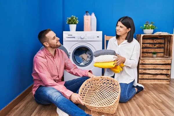家で洗濯をしている若いカップルが横を見て笑って — ストック写真