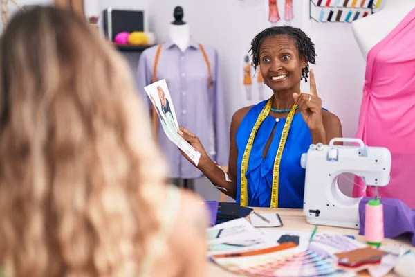African woman with dreadlocks dressmaker designer at atelier with customer smiling with an idea or question pointing finger with happy face, number one