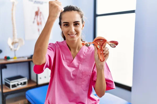 Young hispanic woman holding model of female genital organ at rehabilitation clinic annoyed and frustrated shouting with anger, yelling crazy with anger and hand raised