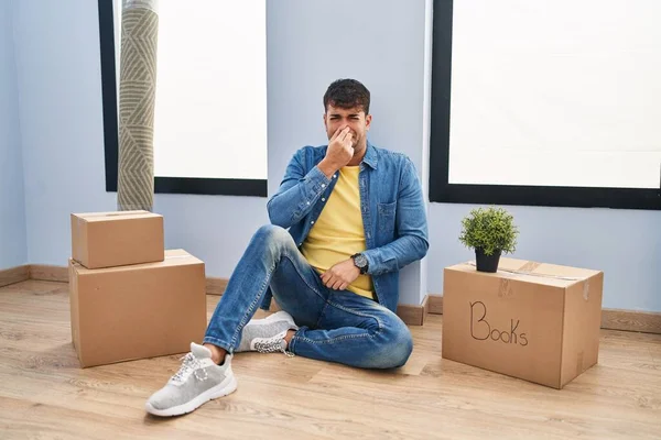 Young Hispanic Man Sitting Floor New Home Smelling Something Stinky —  Fotos de Stock