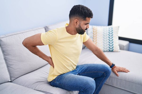 Молодой араб, страдающий от боли в спине, сидит дома на диване
