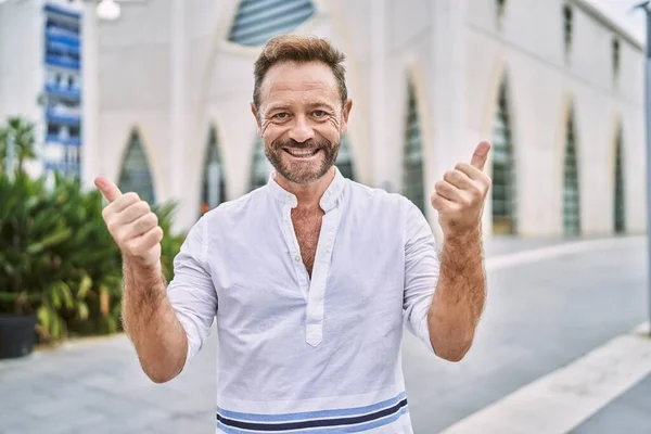 Middle age man outdoor at the city success sign doing positive gesture with hand, thumbs up smiling and happy. cheerful expression and winner gesture.