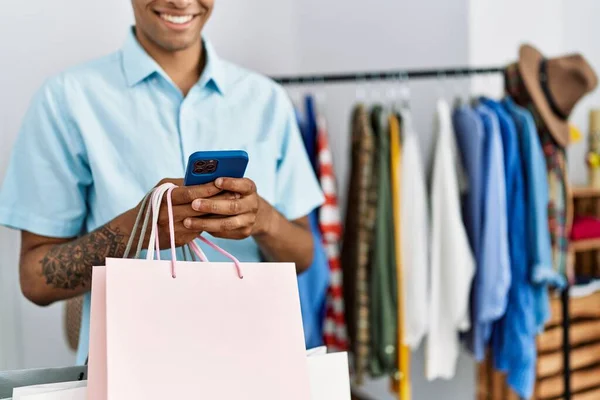 Young Hispanic Man Holding Shopping Bags Using Smartphone Retail Shop — стоковое фото