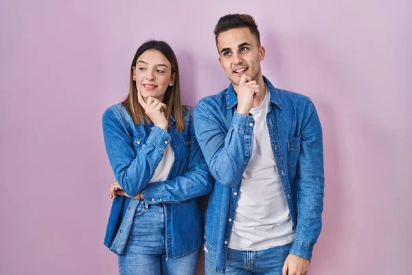 Young Hispanic Couple Standing Pink Background Hand Chin Thinking Question — Stockfoto